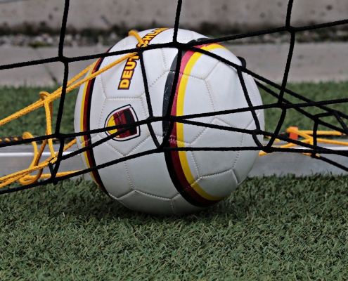 Ein weißer Fußball mit schwarz-rot-gelben Umrandungen liegt in einem Tornetz.