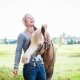 Psychologin Anja Heine schmust lachend mit ihrem Pferd auf einer Weide.