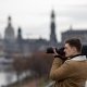Der Workshopleiter im Fokus mit seiner Spiegelreflexkamera fotografiert in die Ferne. Im Hintergrund verschwommen die Skyline von Dresden.