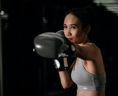 Junge Frau mit einem leichten asiatischen Taint mit Boxhandschuhen beim Training. Dunkler Hintergrund.